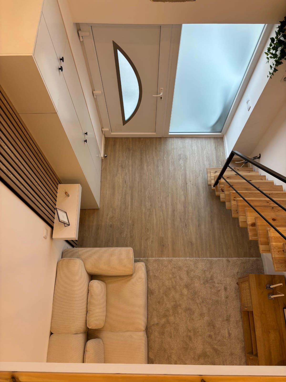 Vista superior da sala e entrada, com porta, escada em madeira, sofá creme e tapete